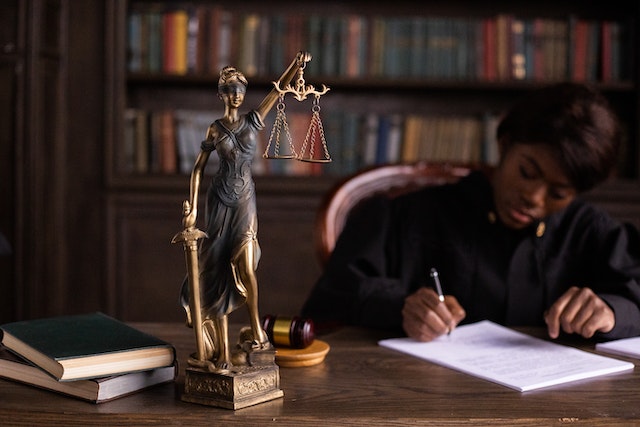 judge working at their desk with a status of lady justice in foreground